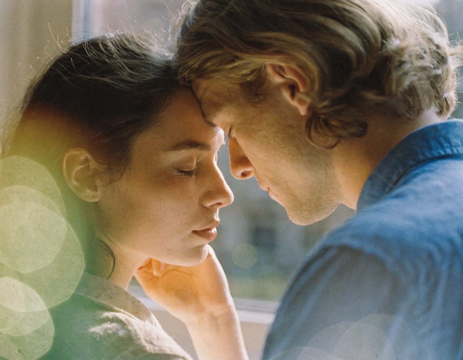 A film still — two faces, foreheads gently together, in soft golden light.